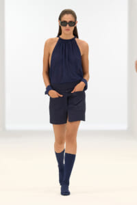 Model walking a runway in a navy halter top, matching shorts, navy knee-high socks, and sunglasses.
