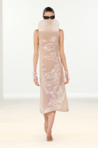 Runway model in a pale beige sequined midi dress with clear gloves and black sunglasses.