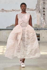 Model walking in a pale pink, voluminous dress with a layered skirt on a runway.