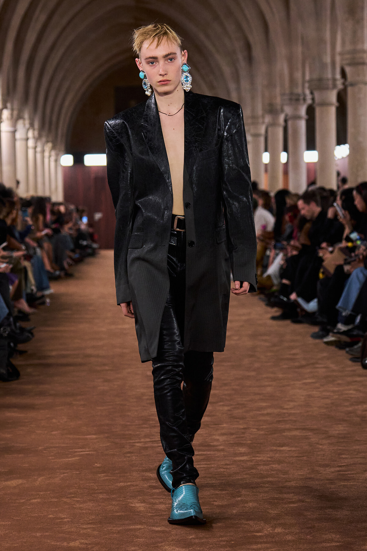 Runway model in an oversized black blazer, black pants, turquoise boots, and bold turquoise earrings.” (informative fashion image)
