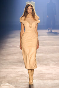 Model walks a cream off-shoulder gown with a circular rose centerpiece, on a fashion runway.