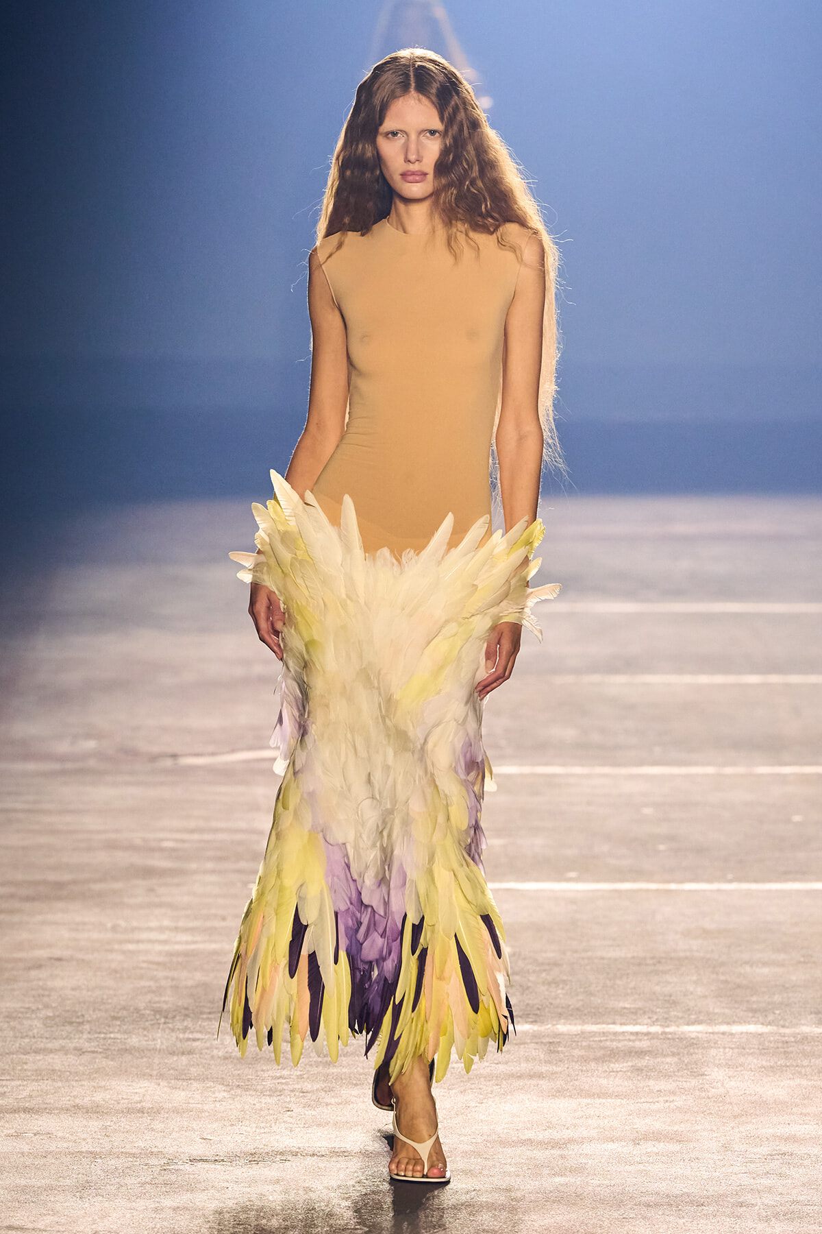 Runway model wearing a nude sleeveless dress with a long, pastel feathered skirt in pale yellow, lavender, and cream colors.