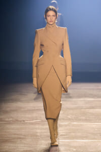 Model walks the runway in a beige tailored double-breasted blazer and matching skirt with knee-high boots.