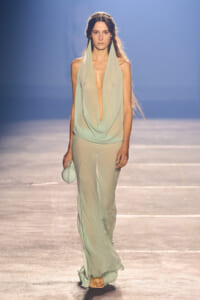 Model walking the runway in a mint green draped halter top with sheer matching pants, carrying a small round mint bag.