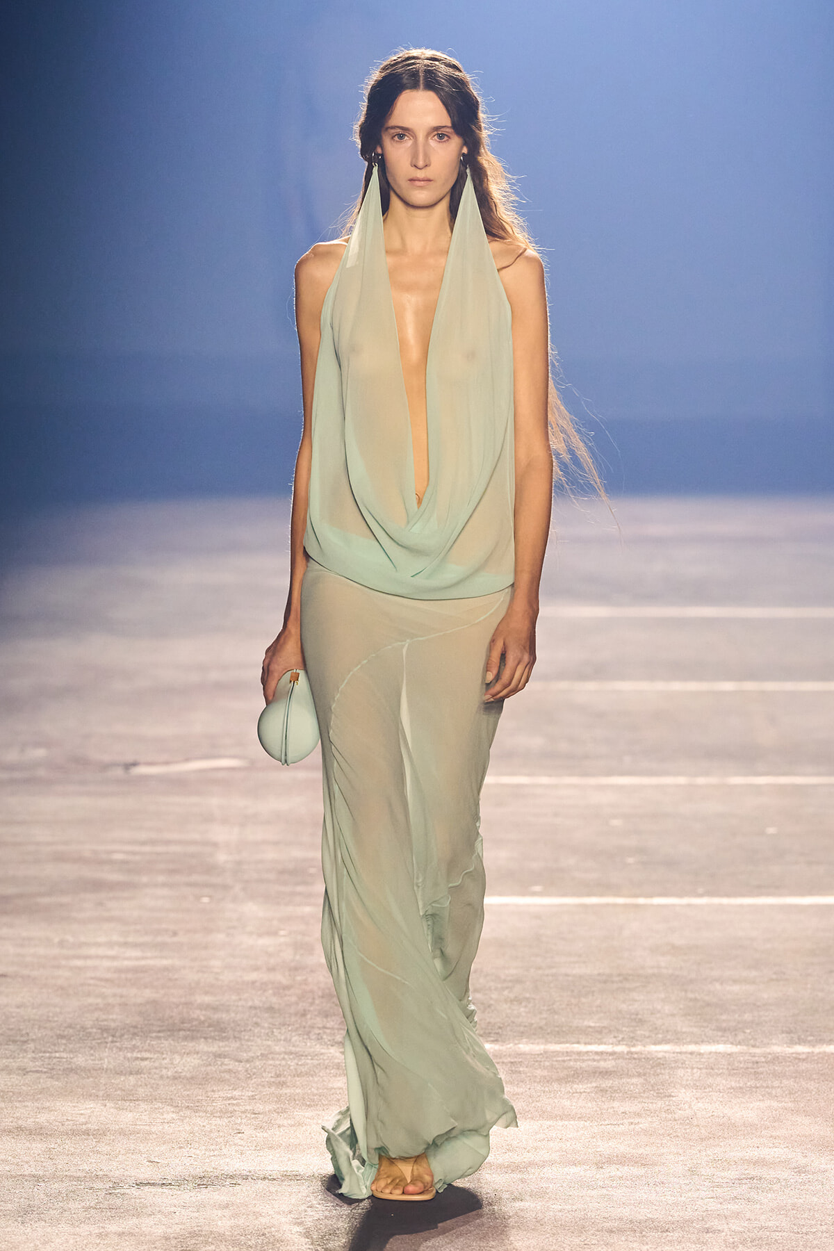 Model walking the runway in a mint green draped halter top with sheer matching pants, carrying a small round mint bag.