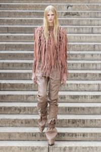 Model wearing a pink fringe top and beige baggy pants standing on concrete steps, facing the camera.