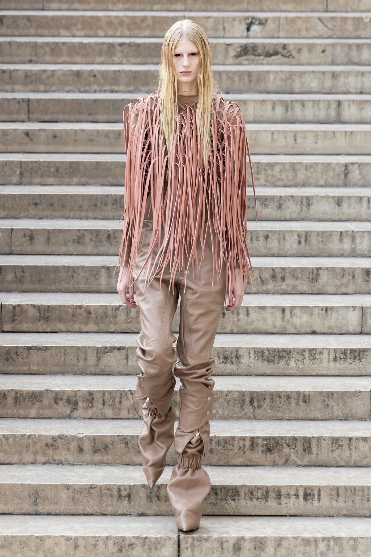Model wearing a pink fringe top and beige baggy pants standing on concrete steps, facing the camera.