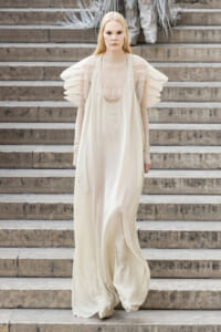 Model in an ivory, flowing gown with sheer puff sleeves walking down stone steps on a runway