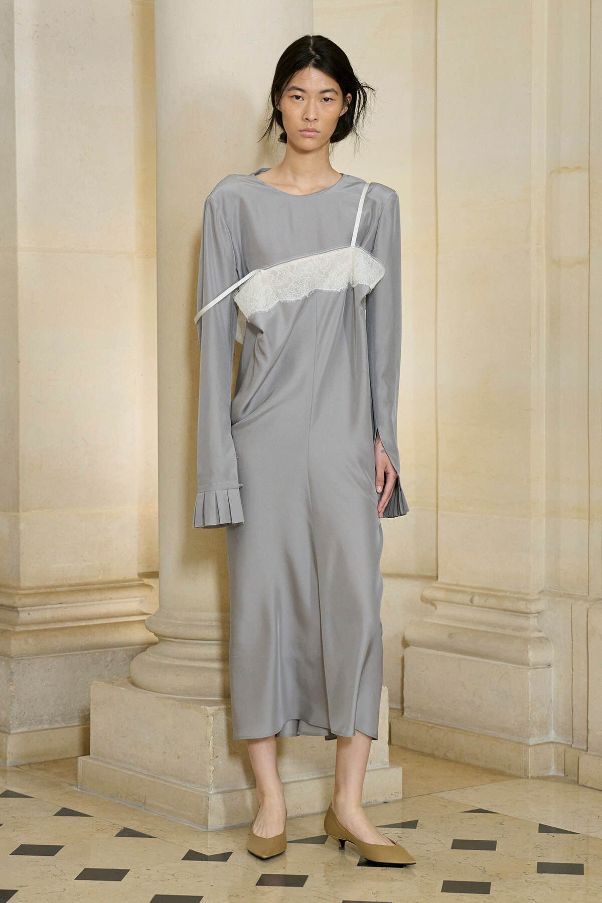 Model wearing a gray midi dress with a white lace bandeau across the chest, thin strap, standing beside stone columns.