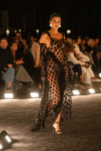 Model wearing a sheer black polka-dot gown with feather details walks the fashion runway.