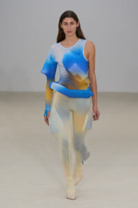 Female model walking a runway in a blue-to-yellow gradient knit bodysuit with matching pants.