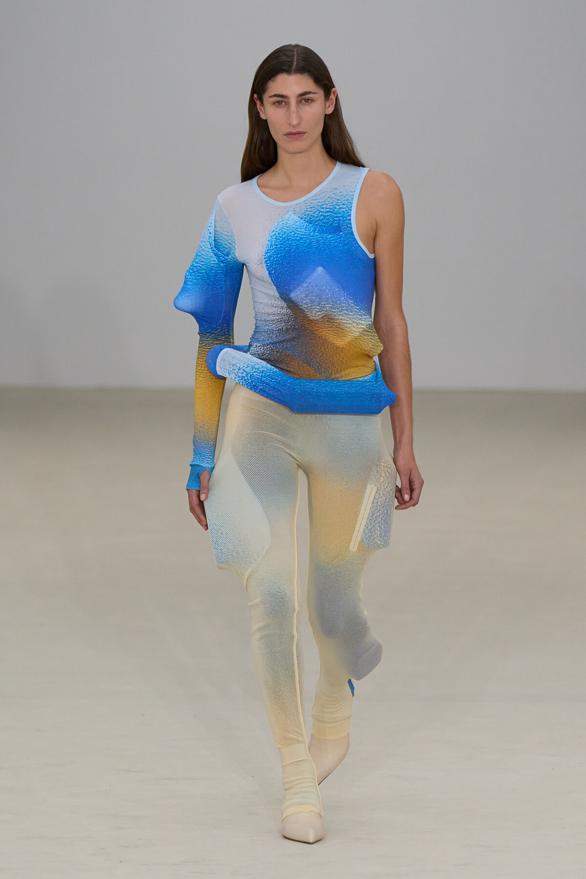 Female model walking a runway in a blue-to-yellow gradient knit bodysuit with matching pants.
