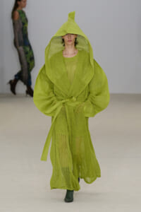 Model walks the runway in a bright lime-green, oversized sheer knit robe with a hood, belted at the waist.
