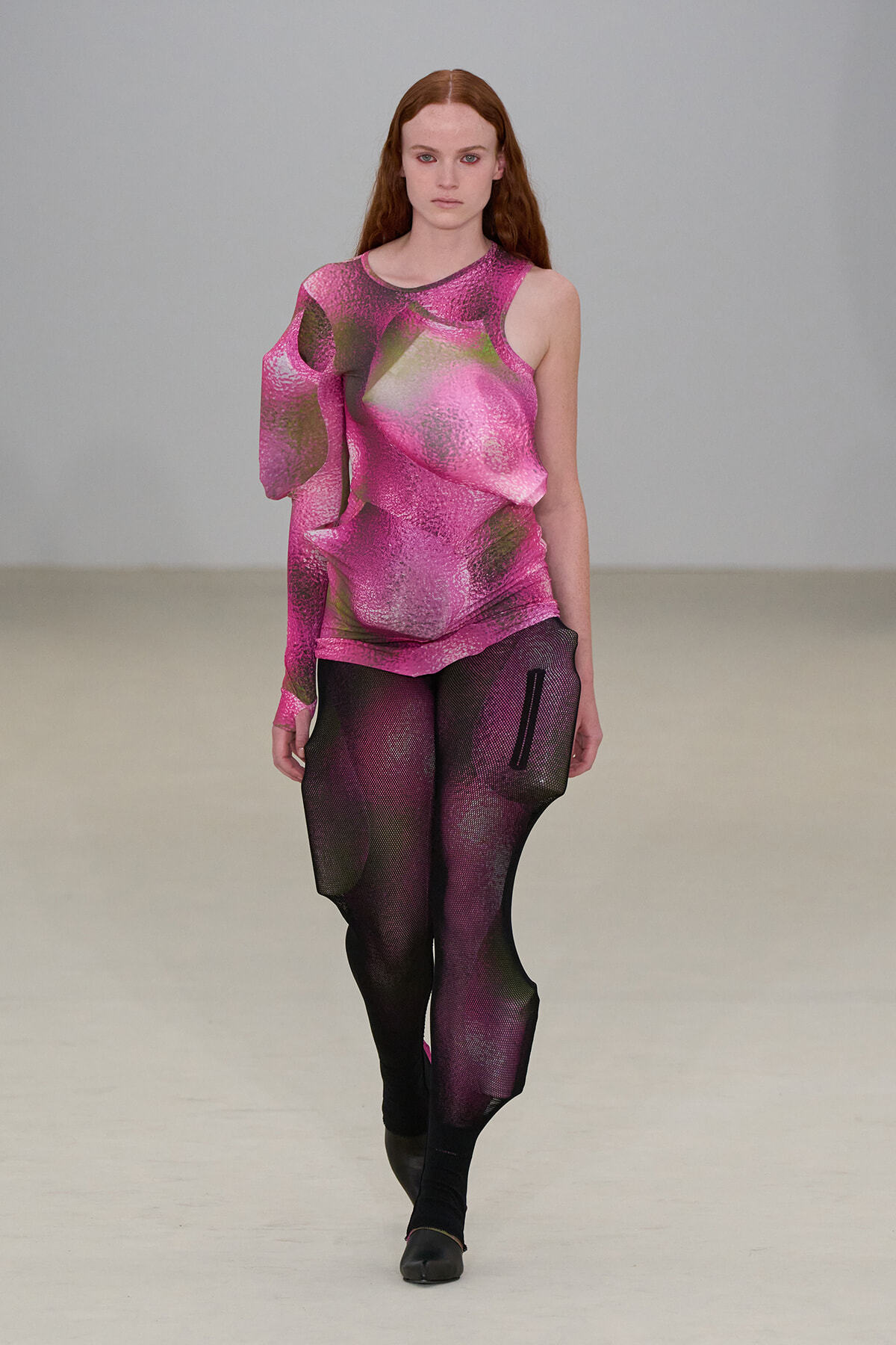 Model walking a runway in a vivid pink metallic one-shoulder top paired with pink-black gradient leggings.