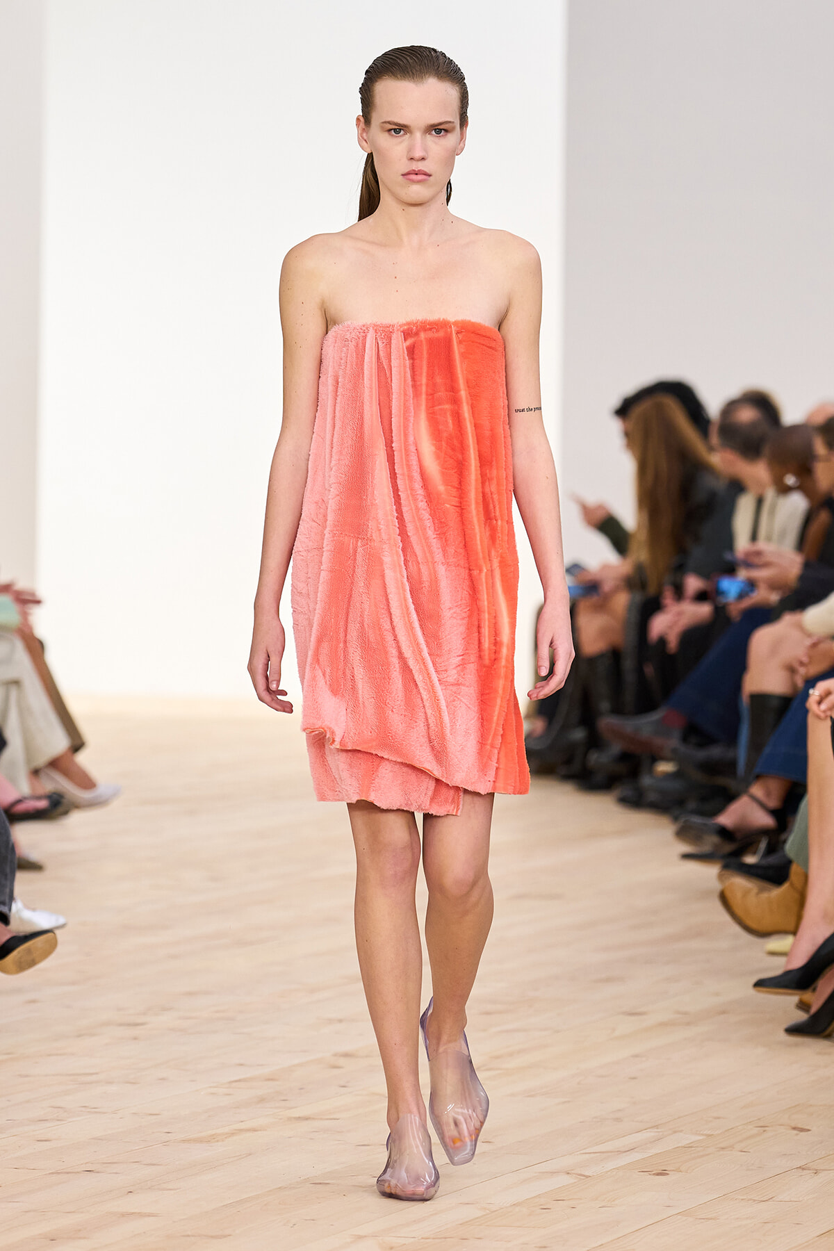 Model walks the runway in a strapless coral-pink textured dress, paired with translucent heels.
