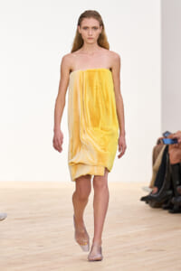 Runway moment: model walking in a strapless, plush yellow towel-inspired dress with clear heeled shoes.