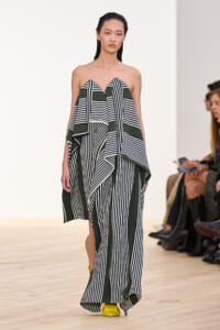 Model on runway wearing a strapless green and black striped draped gown with long, flowing panels.