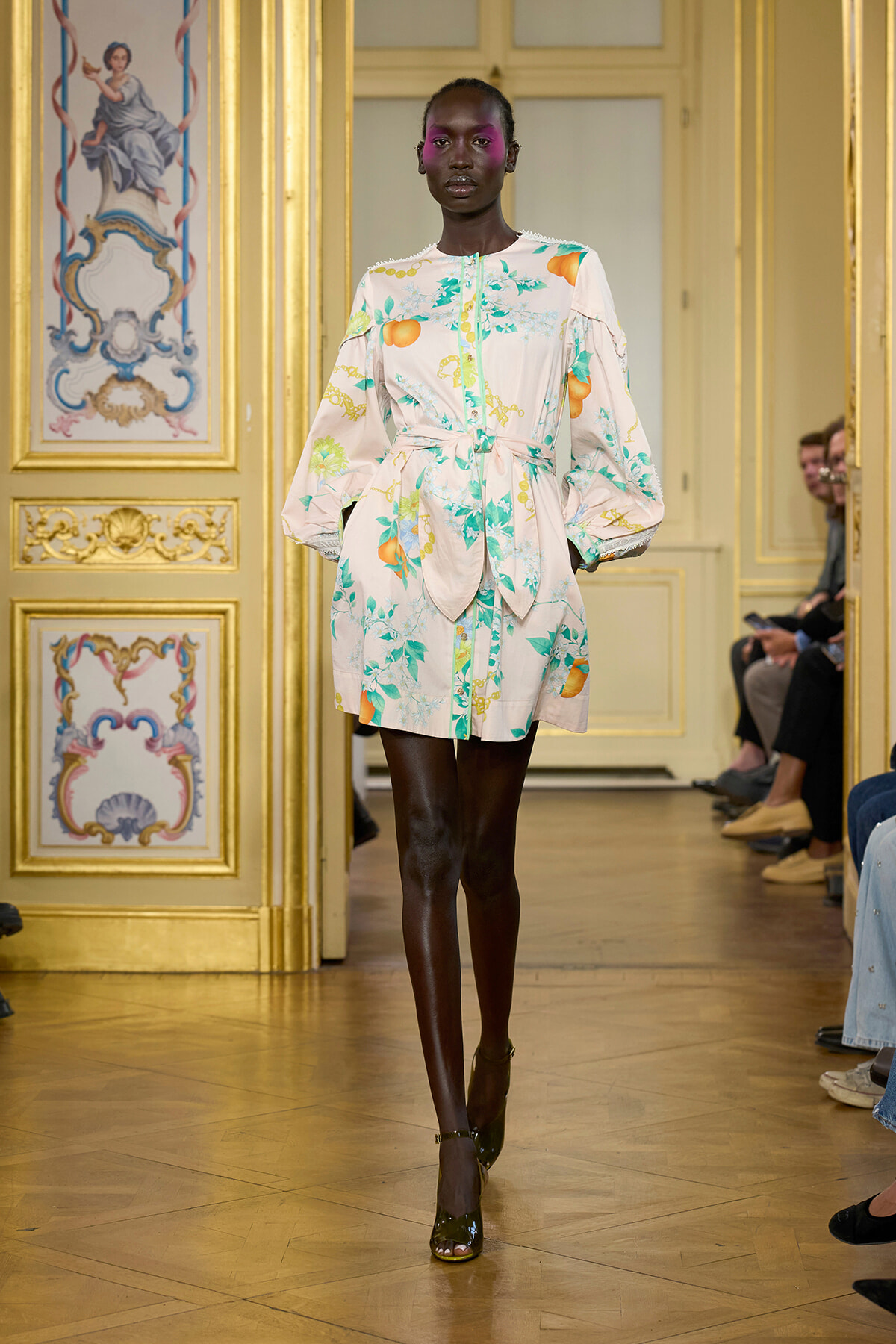 Model in pastel floral dress with a tied waist and puff sleeves walking a gilded runway.