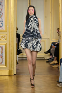 Model walking a fashion runway in a navy‑and‑white abstract‑print halter top with a matching bubble skirt, set in a gilded, ornate room.
