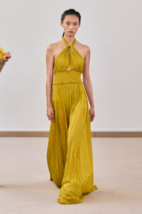Model walks the runway in a mustard yellow halter-neck, twisted top with smocked waist and flowing maxi skirt.