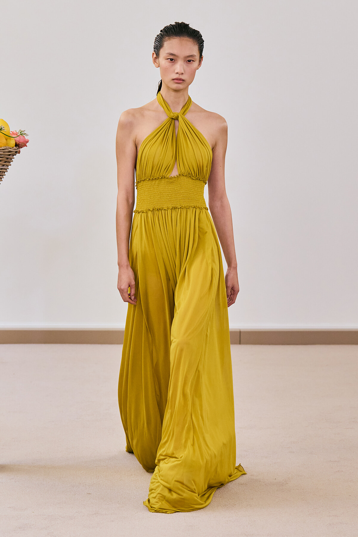 Model walks the runway in a mustard yellow halter-neck, twisted top with smocked waist and flowing maxi skirt.