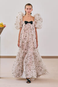 Model wearing a pink floral maxi dress with voluminous puff sleeves and a black front bow, walking in a studio.