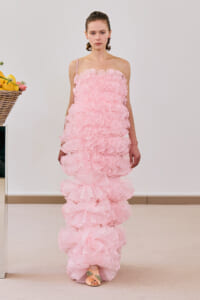 Model wearing a pale pink strap-detailed gown with cascading layered ruffles reaching the floor, in a studio setting.