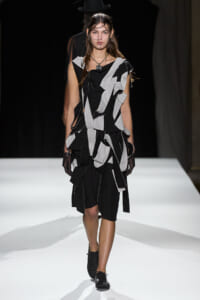 Model walks the runway in a black-and-white geometric patchwork dress made of ragged fabric strips.