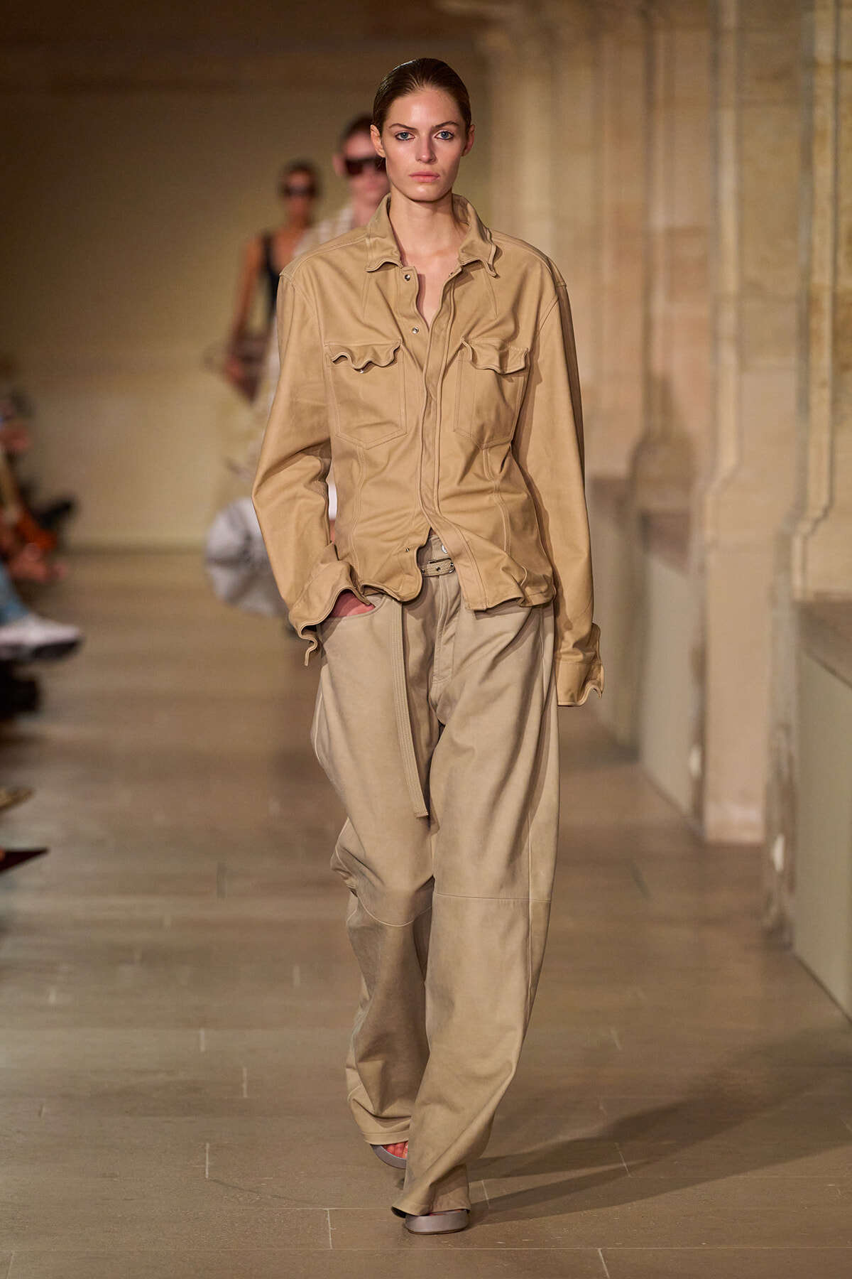 Model walking a beige utility jacket and wide-leg khaki pants on a fashion runway