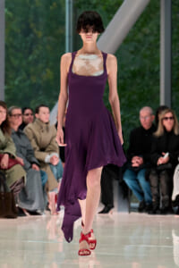 Model walks the runway in a plum purple sleeveless dress with a marbled chest panel and red strappy sandals.