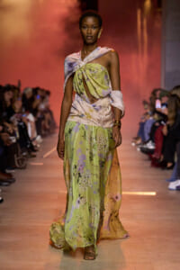 Model walks the runway in a pastel floral maxi dress with a twisted knotted bodice and bare shoulder.