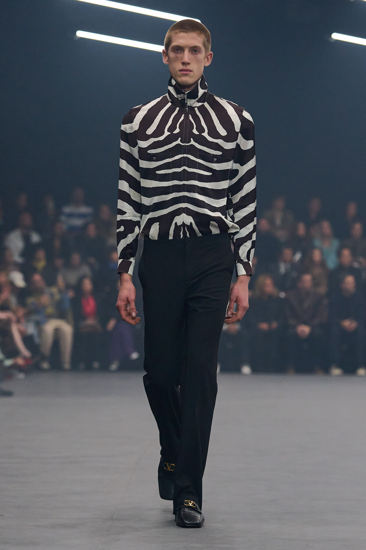 Model walks the runway in a black-and-white zebra-patterned zip-up shirt and black trousers.