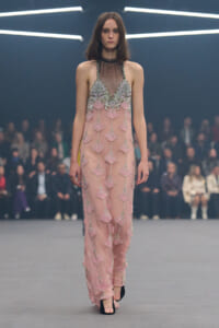 Model walking a pink, bead-embellished gown with a sheer neckline on a runway.