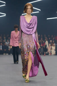 Runway model in a lilac sequined gown with a draped purple shawl and green heeled sandals.