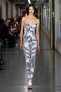 Model walking the runway in a strapless white jumpsuit with navy vertical stripes and white sandals.
