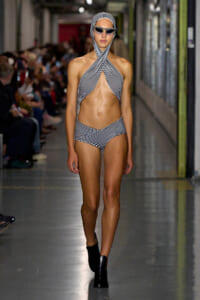 Model walking a fashion runway in a black-and-white striped crisscross bikini with matching head wrap and sunglasses.
