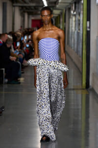 Runway model wearing a blue-and-white striped strapless top with oversized floral-print pants and a large daisy-pattern wrap at the waist