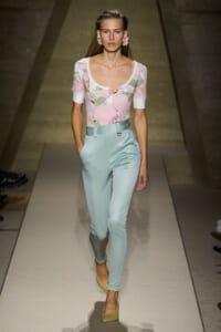 Model walking a runway in a pink floral short-sleeve top and pastel blue high-waisted pants with beige heels.