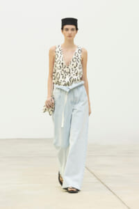 Model walking in a leopard-print sleeveless top with light blue wide-leg jeans and a black hat, holding a leopard-print clutch.