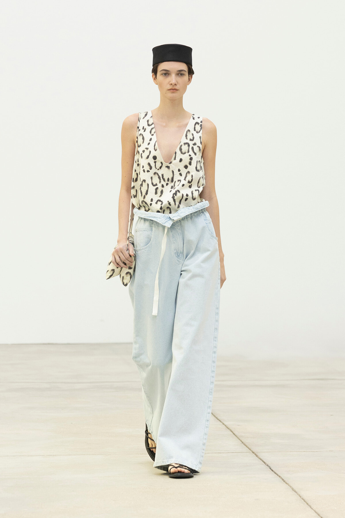 Model walking in a leopard-print sleeveless top with light blue wide-leg jeans and a black hat, holding a leopard-print clutch.