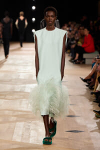 Model walks the runway in a pale mint sleeveless dress with a white feathered hem and emerald-green sandals.