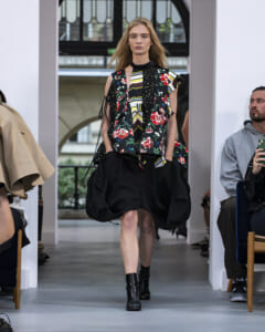 Model walks a runway in a bold, multi-pattern top with a voluminous black bubble skirt and black ankle boots.