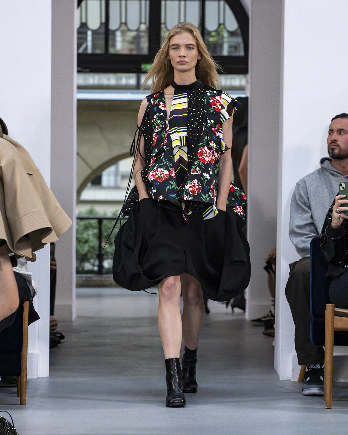 Model walks a runway in a bold, multi-pattern top with a voluminous black bubble skirt and black ankle boots.