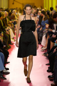 Model walking a pink runway in a black textured halter-neck dress with a ruched bodice.
