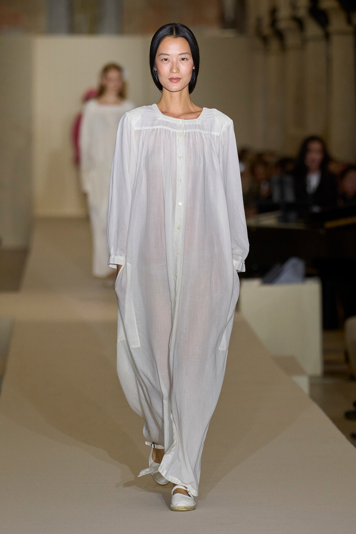 Model walks the runway in an oversized white button-down maxi dress with pockets and white sandals.