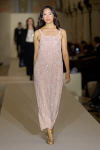 Model walking the runway in a pale pink floral lace dress with thin straps and gold sandals.