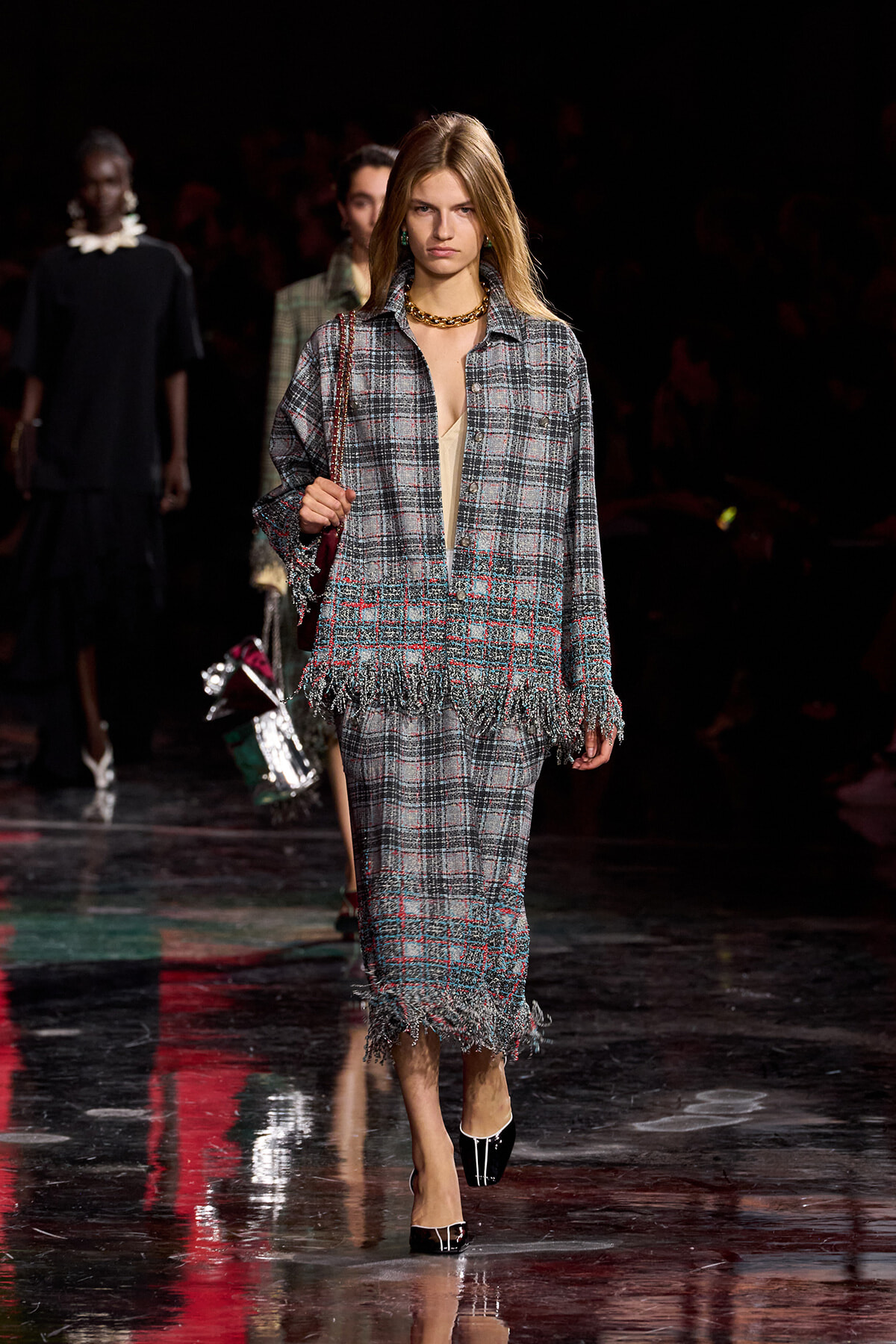 Model walks the runway in a gray plaid fringed suit with a beige top, gold chain necklace, and black patent heels.