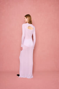 Back view of a woman in a long lavender knit dress with a teardrop back cutout against a pink textured backdrop