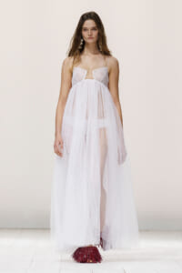 Model walking a fashion show in a sheer white tulle gown with thin straps and a full skirt.