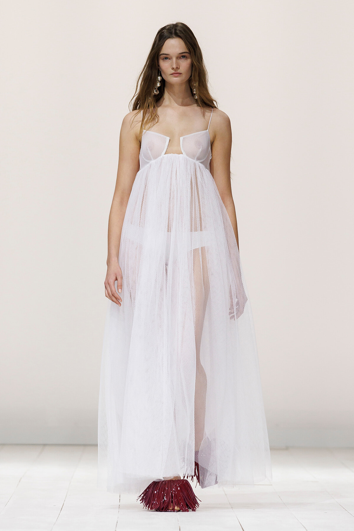 Model walking a fashion show in a sheer white tulle gown with thin straps and a full skirt.